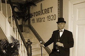 Foto von einem Mann in Anzug und mit Hut vor dem TORKRET Logo