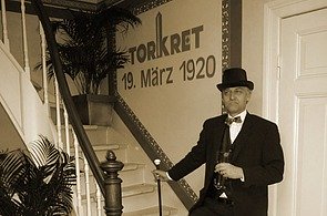 Foto von einem Mann in Anzug und mit Hut vor dem TORKRET Logo