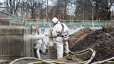 Foto von einer Person in weißem Schutzanzug mit Spritzbetonlanze in der Hand